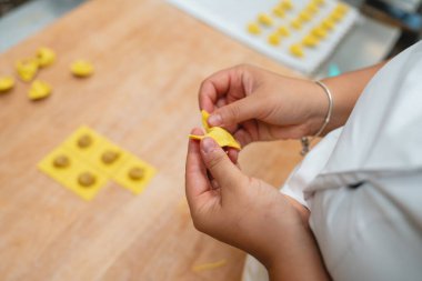 Yakın plan el yapımı taze ev yapımı tortellini makarnayı ahşap bir masada dikkatlice şekillendiriyor.