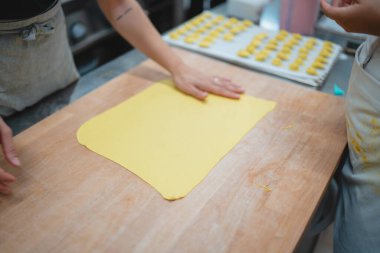 Profesyonel bir mutfak ortamında ahşap bir tahtanın üzerinde taze makarna hamuru şekillendiren eller.