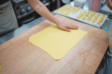 Şefin elleri ahşap masaya taze makarna hamuru bastırarak ravioli yapmaya hazırlanıyor.