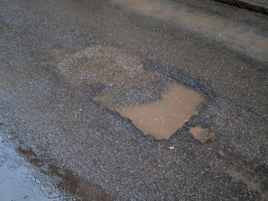 Yağmurdan sonra oluşan su birikintileriyle asfalt yol yüzeyinde aşınma ve yıpranma görülüyor.