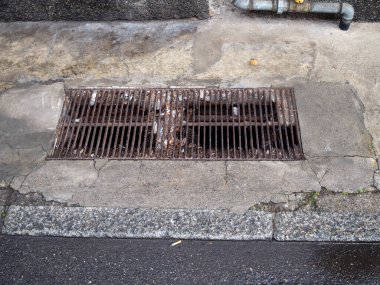 Çatlak beton kaldırımdaki rögarı kaplayan paslı metal ızgara.
