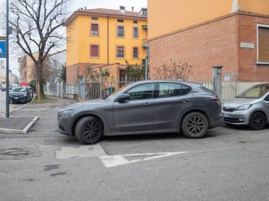 Cremona, İtalya 6 Şubat 2026 Lüks Alfa Romeo Stelvio SUV parlak gri renkte, şehir caddesinde, tuğla ve sarı renkli modern konut binalarıyla çevrili.