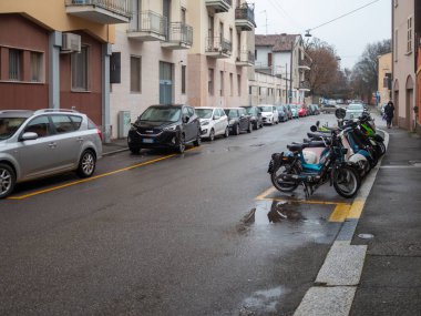 Cremona, İtalya 6 Şubat 2026. Islak Sokak, park halindeki araçlar ve motosikletlerle İtalyan kentsel alanındaki bulutlu bir günde konut binaları ve kaldırımların arka planına karşı.
