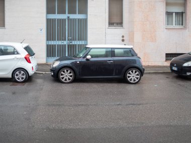 Cremona, İtalya 6 Şubat 2026 Mini Cooper şehir yaşam tarzını ve yağmurlu banliyö trafiğini yansıtan küçük hatchback tasarımlı konut binalarının yanındaki ıslak bir şehir sokağına park etti.