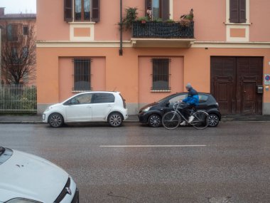 Cremona, İtalya 6 Şubat 2026 Urban sokak sahnesinde Volkswagen Up ve Toyota Aygo arabalarını park etmiş bir bisikletçinin bir apartman cephesi boyunca geçişi