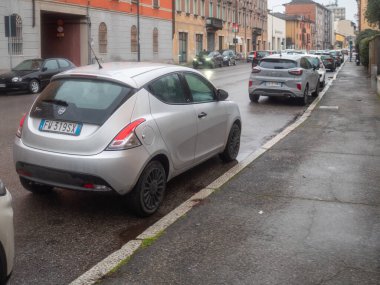 Cremona, İtalya 6 Şubat 2026 Lancia Ypsilon hatchback ıslak bir şehir sokağına park etmiş ve yanından bir Ford Puma geçiyor.