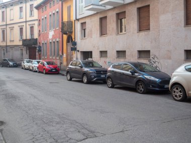 Cremona, İtalya 6 Şubat 2026 Dar Avrupa şehir caddesi park edilmiş arabalar, aşınmış asfalt ve çatlamış kaldırımlar eski konut binaları ve kaldırımların yanında