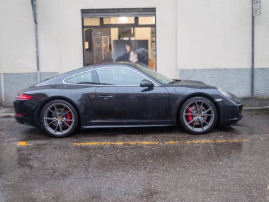 Cremona, İtalya 6 Şubat 2026 Porsche 911 Carrera S siyah 991.2 nesil park etmiş, parlak tasarımı, kırmızı fren kalibreleri ve ıslak bir sokakta alaşım tekerlekleri sergiliyor.