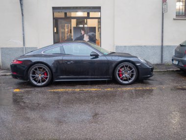 Cremona, İtalya 6 Şubat 2026 Porsche 911 Carrera S siyah 991.2 nesil park etmiş, parlak tasarımı, kırmızı fren kalibreleri ve ıslak bir sokakta alaşım tekerlekleri sergiliyor.