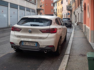 Cremona, İtalya 6 Şubat 2026 Beyaz BMW X2 xDrive18d SUV İtalya 'da yağmurlu bir iskan caddesinde park etmiş, yağmurda şehir mimarisi ve şehir ulaşımının görüntülerini yakalıyor.