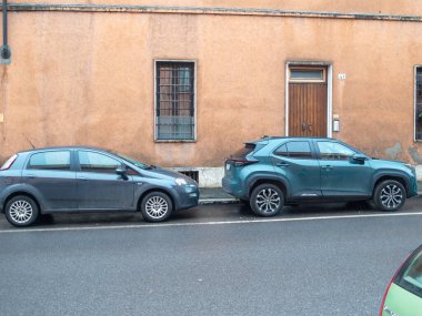 Cremona, İtalya 6 Şubat 2026 Fiat Punto ve Toyota Yaris Cross bir kaldırım kenarında park halindeki küçük arabalar, yıpranmış bir şehir cephesine karşı, günlük ulaşım