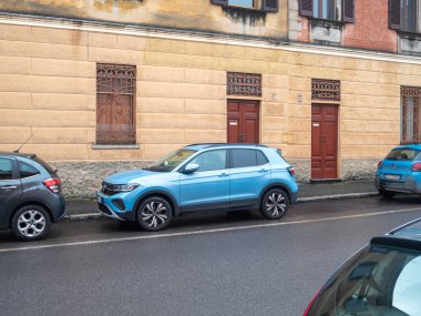 Cremona, İtalya 6 Şubat 2026 Volkswagen T Cross mavi kompakt SUV kahverengi kapılı eski bir apartmanın önündeki bir şehir caddesine park edilmiş.