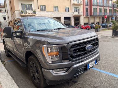 Çağdaş koyu gri bir Ford F-150 kamyonet, arka planda binalar bulunan Avrupa kentinin asfalt bir caddesinde park halinde.