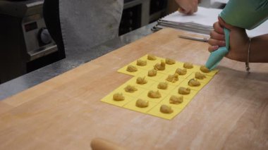 İki kadın taze tortelli yapmaya odaklanmış, biri boru dolgusu ve diğeri hamur kareleri yerleştiriyor, sanatsal gıda üretimi sergiliyorlar.