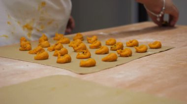 Close-up view of small, handmade tortelli pasta dough portions arranged on a baking sheet, ready for cooking