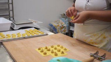 Yetenekli eller, hassas tortelli 'yi şekillendirir. Mutfak ortamında makarna yapmanın sanatsal sürecini gözler önüne serer.