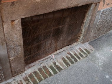 Cremona, Lombardy, İtalya 'daki bodrum penceresi, kentin tarihsel mimari karakterini yansıtan engebeli bir taş çerçeve, paslı demir ızgara ve aşınmış tuğla işçiliği içeriyor.