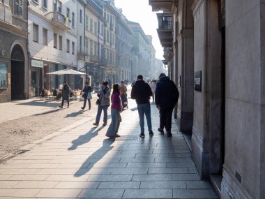 Cremona, İtalya - 7 Ocak 2026 Cremona, Lombardy, İtalya 'da güneşli bir cadde boyunca yürüyen yayalar, kaldırımda uzun gölgeler oluşturarak günlük yaşamı ve tarihi mimariyi gözler önüne serdiler.