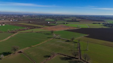 Po Vadisi 'nin kırsal arazileri açık mavi gökyüzü altında yayılıyor. Yama tarımlarını, sulama kanallarını ve verimli tarım yaptığını gösteren dağınık çiftlik binalarını gösteriyor.