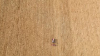 Traktör kuru bir alanda yeni sürülmüş toprağı düzleştiriyor, bahar tohumlama hazırlıkları sırasında toprağı işliyor, geleneksel tarım ve kırsal çalışmaları vurguluyor