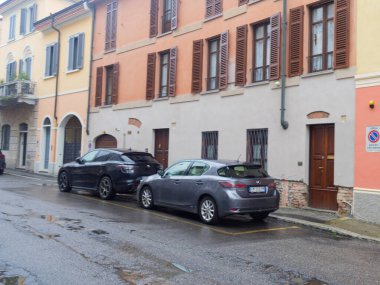 Cremona, İtalya - 3 Şubat 2026 koyu renkli bir SUV ve gri bir hatchback, arka planda panjurları olan yağmurlu bir sokakta yan yana park edilmiş durumdalar.