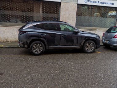 Cremona, İtalya - 3 Şubat 2026 Parlak, koyu renkli bir SUV ıslak, gri asfalt bir yolda park edilmiş, bulutlu gökyüzünü ve çevresindeki kentsel çevreyi yansıtıyor