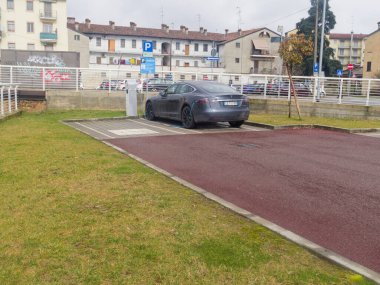Cremona, İtalya - 3 Şubat 2026 Modern bir elektrikli sedan bulutlu bir günde bir şarj istasyonuna bağlandı.