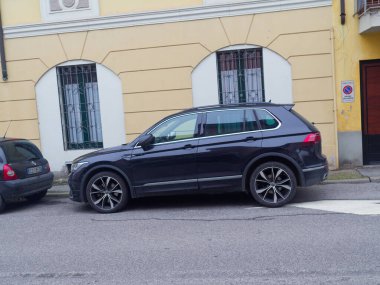 Cremona, İtalya - 3 Şubat 2026 Modern bir koyu mavi Volkswagen Tiguan SUV sarı duvarlı ve kemerli pencereli bir binanın önündeki asfalt yolda park edilmiştir.
