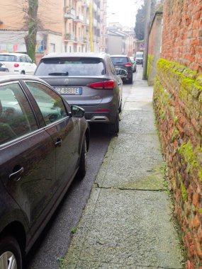 Cremona, İtalya - 3 Şubat 2026 Gri bir MG SUV dar kaldırımlı ve yosun kaplı tuğla duvarlı bir sokakta park halinde.