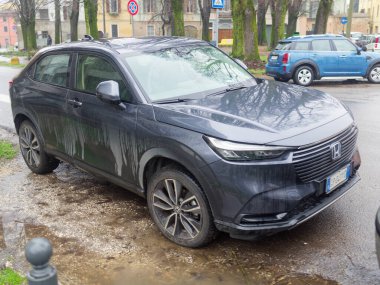 Cremona, İtalya - 3 Şubat 2026 Honda HR-V e: HEV hibrit SUV ıslak şehir kaldırımlarında su birikintileri ve kir ile park etmiş, modern Japon geçiş tasarımı, verimliliği ve günlük şehir hareketliliğini vurguluyor