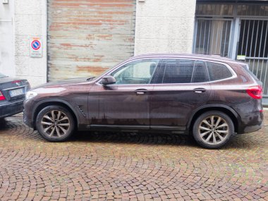 Cremona, İtalya - 3 Şubat 2026 Pürüzsüz, koyu kahverengi bir BMW X3 SUV ıslak, dokulu bir kaldırım taşı caddesinde park halinde, yan profilini gözler önüne seriyor.