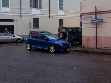 Cremona, İtalya - 3 Şubat 2026 Renault Clio, arka planda diğer araç ve binalarla birlikte ıslak bir asfalt sokağa park edilmiştir.