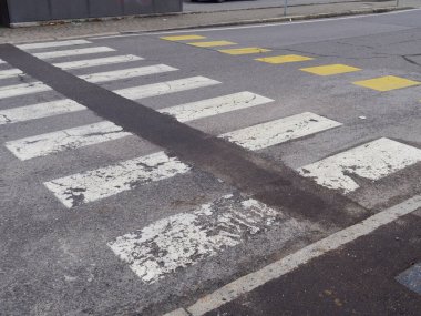 Ortasında koyu bir şerit olan soluk bir yaya geçidinin yakın çekimi, şehir sokaklarında aşınma ve yırtılma olduğunu gösteriyor.