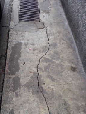 Yakınlarda belirgin bir çatlak ve drenaj ızgarası gösteren hasarlı beton bir yüzeye yakın çekim.