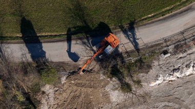 Turuncu bir kazıcı, yüksek bir hava perspektifinden yakalanan bir inşaat sahasındaki toprak taşıma operasyonlarıyla aktif olarak meşgul.