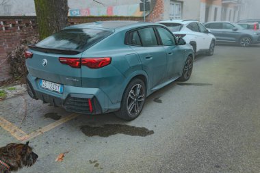 Cremona, İtalya - 6 Şubat 2026 BMW X2 sDrive18d M Sport, Cape York Green 'de modern bir tasarım ve varlığını gözlemleyen bir köpeğin yer aldığı şehir caddesinde park halinde.
