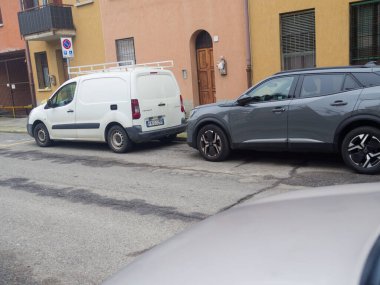 Cremona, İtalya - 26 Şubat 2026 Beyaz ticari bir minibüs ve modern gri bir SUV apartman binalarının önündeki asfalt bir sokakta yan yana park edilmiş.