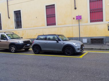 Cremona, İtalya - 26 Şubat 2026 Siyah çatılı modern gümüş renkli bir Mini Cooper asfaltlı bir sokakta park halinde, arkasında gümüş rengi bir Land Rover Discovery var.