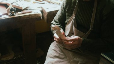 Eski bir İtalyan Luthier Stüdyosu 'nda bir zanaatkarın elleri, hassas aletlerle ahşap bir keman tomarını şekillendirir.