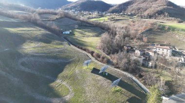 Morfasso, Piacenza 'daki kırsal bir arazinin havadan görünüşü, arka planda bir ev kümesi bulunan çimenli bir yamaçtaki güneş panelleri