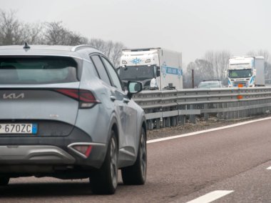 Venedik, A4 otoyolu, İtalya - 25 Şubat 2026 İtalya 'da yoğun bir Autostrada A4' e binen gümüş rengi Kia Sportage, büyük kamyonlar ve diğer araçlarla bulutlu bir gökyüzü altında yolu paylaşıyor.