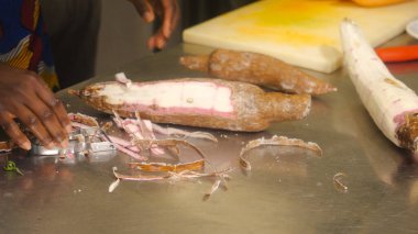 Afrikalı eller, metal bir yüzeye kabuk soyarak geleneksel yemekler ve ticari mutfak ortamında tatlı patates çorbası için taze malzemeler hazırlıyorlar.