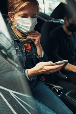 Telefonla konuşan bir kadın virüs bulaşmasını önlemek ve koronavirüs zamanında hastalığın yayılmasını önlemek için yüz maskesi takarak arabada oturuyor.