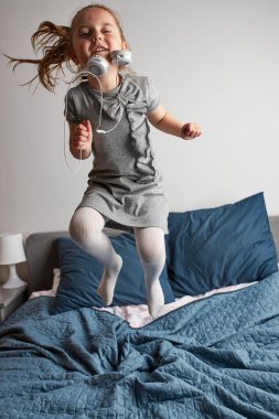 Kulaklıkla şarkı söyleyen küçük kız kendini gerçek bir şarkıcı gibi gösteriyor. Çocuk zıplayarak, dans ederek, yatakta müzik dinleyerek eğleniyor.