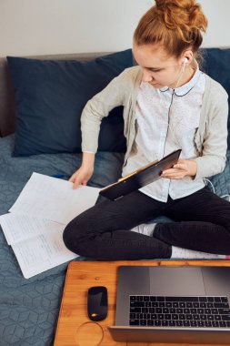 Sınıfı olan genç bir kız öğrenci, internetten öğreniyor, uzaktan ders izliyor, profesörü dinliyor, karantina sırasında okuldan arkadaşlarıyla konuşuyor. Laptop, kulaklık, kitap ve el kitabı kullanan genç bir kız.