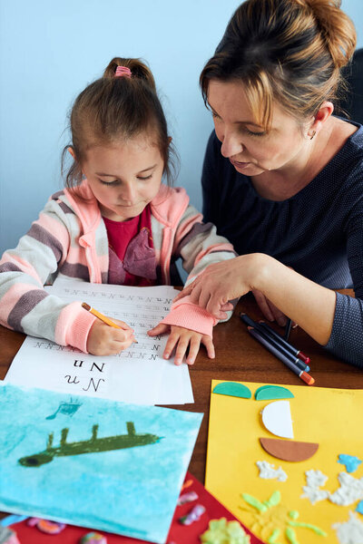 Little girl preschooler learning to write letters with help of her mother. Kid writing letters, drawing pictures, making stuff with paper, doing a homework. Concept of early education