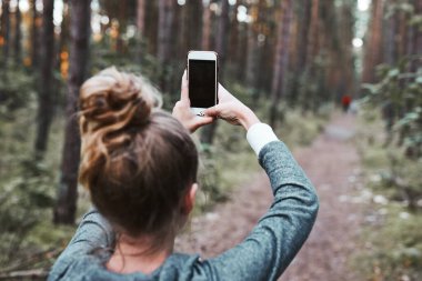 Yaz tatilinde ormanda yürürken akıllı telefon kullanarak fotoğraf çeken genç bir kadın. Akıllı telefon tutan bir kızın arka planı