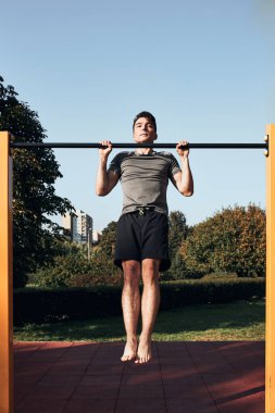 Modern bir jimnastik parkında egzersiz yaparken barfiks çeken genç bir adam. Spor giyinen adam.