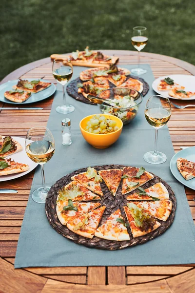 Dinner in a home garden. Pizza, salads, fruits and white wine on table in a orchard in a backyard