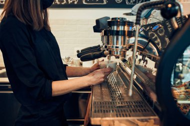 Barista kahve makinesini kullanarak kahve yapan bir bardağa kahve dolduruyor. Kadın barmen espresso yapıyor, kahve hazırlıyor. Bir kafede çalışan genç bir kadın.